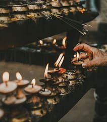 gallery-4 Hand lighting oil lamps during a traditional ritual with incense sticks, creating a spiritual and serene atmosphere.