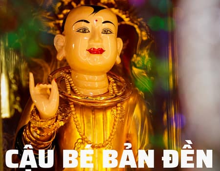 Gilded statue of a boy deity wearing beaded necklaces and bangles with text CẬU BÉ BẢN ĐỀN displayed below.